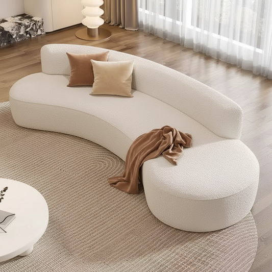 White curved sofa with cushions and a blanket in a living room setting.