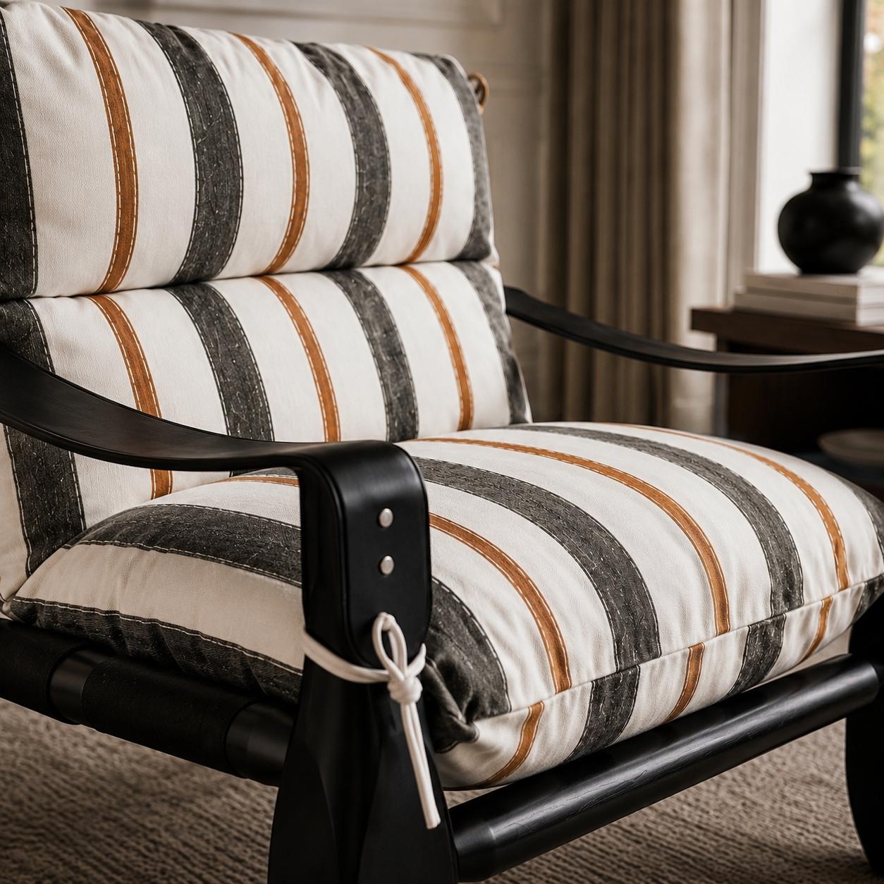 Designer armchair with striped upholstered cushions, a black finished wood frame and leather strap detailing in a luxury living room.