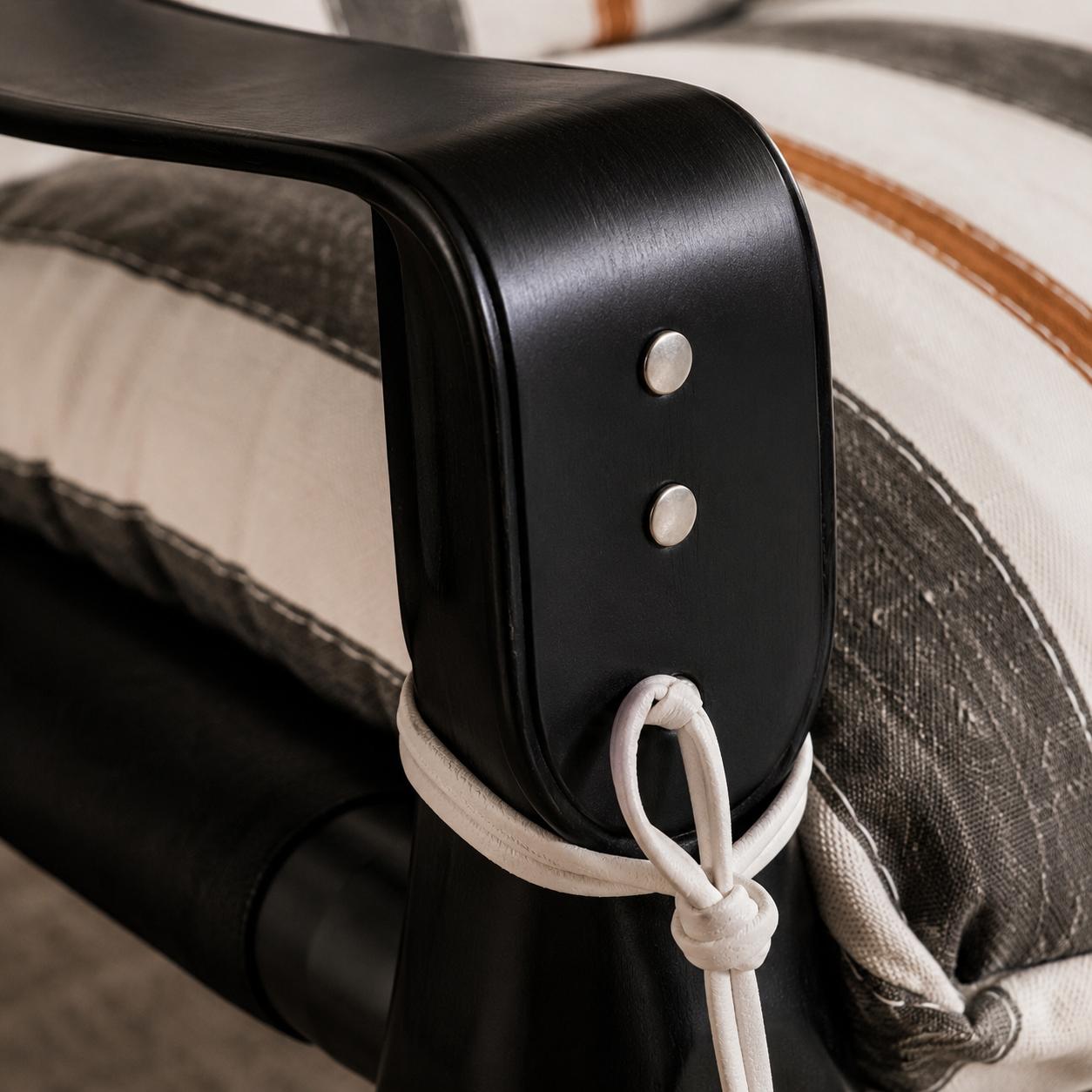 Designer armchair with striped upholstered cushions, a black finished wood frame and leather strap detailing in a luxury living room.