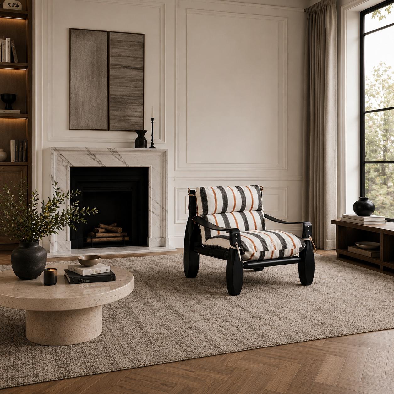Designer armchair with striped upholstered cushions, a black finished wood frame and leather strap detailing in a luxury living room.